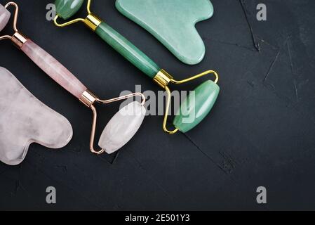 Facial jade massage rollers and gua sha massagers made from natural jade and rose quartz stone on black background, top view Stock Photo