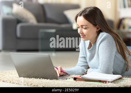 Satisfied student e-learning using laptop lying on the floor at home Stock Photo