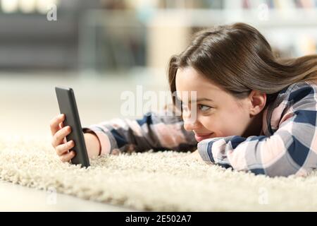 Happy teen checking smart phone content lying on a carpet in the living room at home Stock Photo