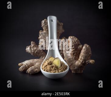 Ginger root and ginger powder in a spoon isolated at black background, close-up. Stock Photo