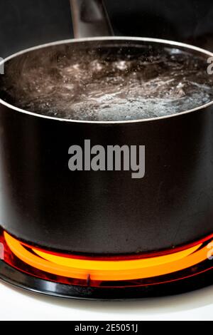 Vertical shot of water boiling in a black pot on a hot stove burner. Stock Photo