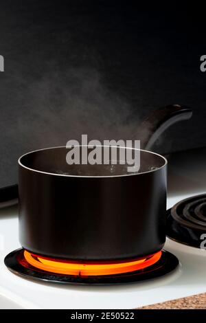 Vertical shot of water boiling in a black pot on a hot stove burner. Stock Photo