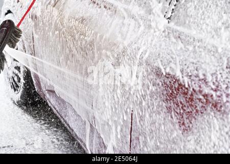 Red car washed in self serve carwash, detail on white soap foam spraying from high pressure hose onto side door Stock Photo