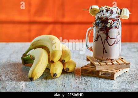 Banana milk shake with cream, chocolate and branch of bananas on the marble background Stock Photo
