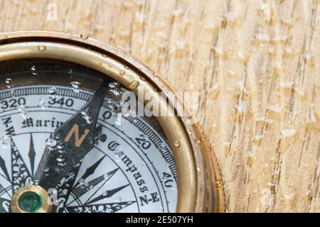 Old Fashioned compass covered in water droplets pointing to north on a wooden deck plank Stock Photo