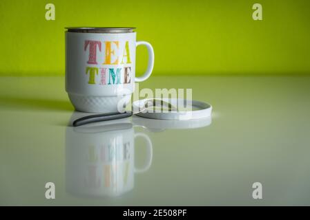 White cup of tea with slogan 'Tea time' reflected on a table with a green background Stock Photo