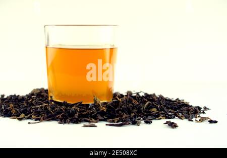 Hot golden, yellow tea in a clear white glass with dried tea leaves isolated on white background. Any hot tea beverage concept. Stock Photo