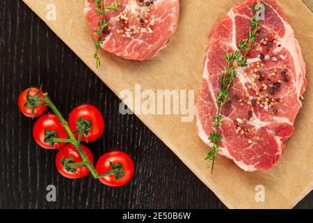 freshly chopped raw pork steaks with spices and thyme on a sheet of parchment. near ripe red tomatoes Stock Photo