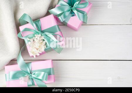Gifts in pink packaging with ribbons and a sweater on a white wooden background. Stock Photo