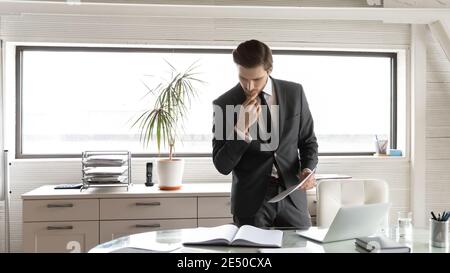 Thoughtful businessman touching chin, checking financial documents in office Stock Photo