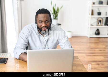 Attractive young African American guy purchasing electronic items online, booking tickets for the conference, buying groceries from the website, a Stock Photo