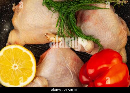 Raw chicken thighs laying in grill pan with lemon, bell pepper, greens, and garlic . Top view close-up Stock Photo