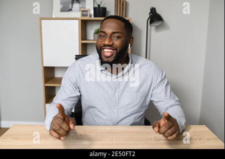 Young and handsome African-American businessman is sitting at the desk and pointing at the camera, showing that you are the perfect candidate for the Stock Photo