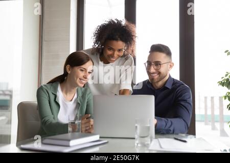 Three happy diverse colleagues working on project together, using laptop Stock Photo