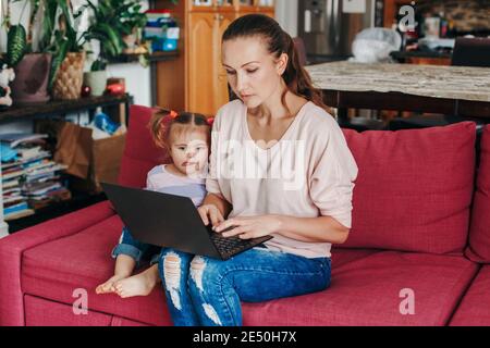 Caucasian mother with baby working on laptop from home. Workplace of freelance business woman with kid toddler. Video chat call. Stay at home single Stock Photo