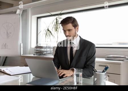 Focused businessman wearing suit using laptop, typing on keyboard Stock Photo