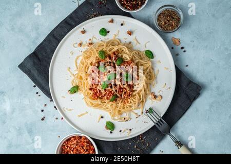 Pasta and tomato sauce with minced meat, basil, cheese and nuts in a flat plate on a gray background. Stock Photo