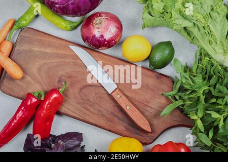 Fresh vegetables. Cabbage, onion, lemon, lime, greens on gray background with wooden board and knife Stock Photo