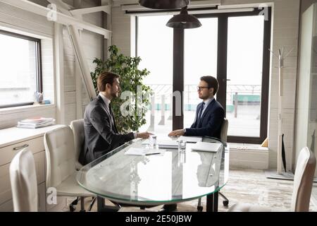 Two confident businessmen sitting at table in boardroom, discussing project Stock Photo