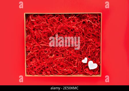 Opened gift box with shredded red paper on plain red background. Flat lay, top view. Box for your product replacement. Valentine's Stock Photo