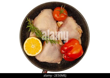 Raw chicken thighs laying in grill pan with lemon, bell pepper, greens and garlic isolated on white background. Top view Stock Photo