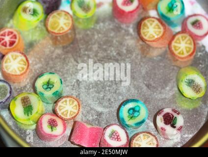 Half-empty tin can with multicolored lollipops with different flavors on a white table, space for text. Candy sweets with drawing of fruits for kids Stock Photo