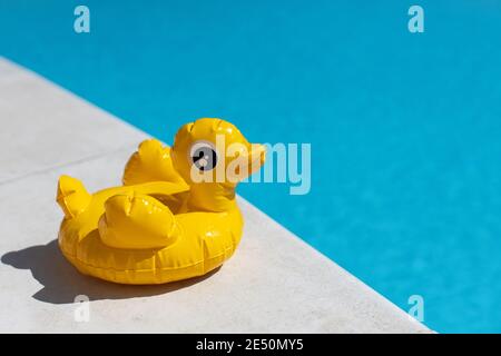 Inflatable yellow mini duck, cocktail stand near swimming pool on bright sunny day, copy space. Concept of summer vacation, entertainment, water, air, Stock Photo