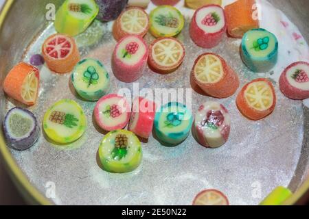 Half-empty tin can with multicolored lollipops with different flavors on a white table, space for text. Candy sweets with drawing of fruits for kids Stock Photo