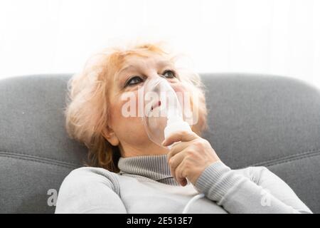 Elderly woman using asthma machine on light background Stock Photo
