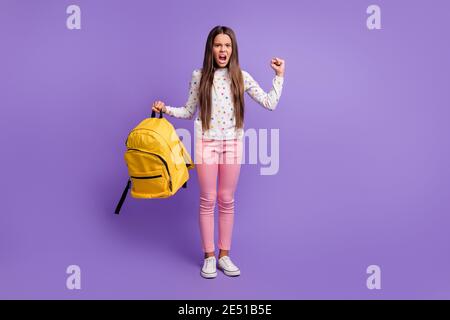 Full length body size photo of angry irritated girl keeping yellow backpack shouting showing fist isolated on vibrant purple background Stock Photo
