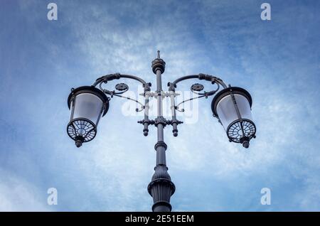 Street lamp seen from below with the blue sky in the background with some clouds. Stock Photo