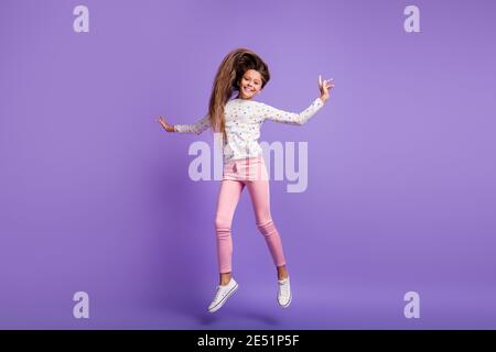 Full length body size photo schoolgirl laughing jumping throwing long hair air in casual outfit isolated on vibrant purple color background Stock Photo