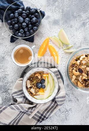 Overhead view of two granola bowls next to a foamy coffee cup, some orange and apple slices in the middle and a glass jar full of fresh cranberries. Stock Photo