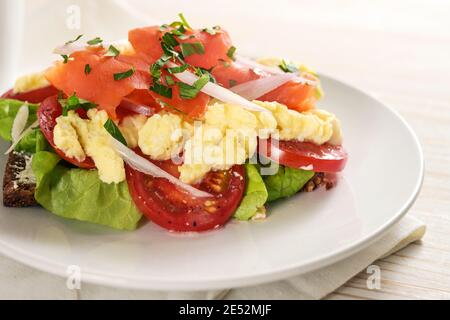 Smoked salmon and scrambled eggs on whole meal bread with tomatoes and lettuce, healthy sandwich meal on a white plate, selected focus, narrow depth o Stock Photo
