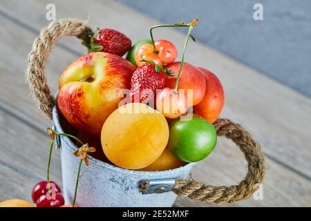 Bucket of fresh summer fruits on wooden table Stock Photo