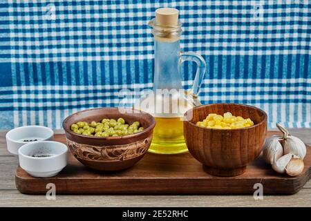 Bowls of boiled sweet corn and green peas, spices, oil, and vegetables on a wooden board with a tablecloth Stock Photo