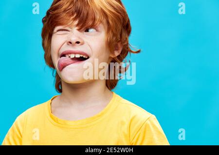 grimacing red-haired boy showing tongue squinting one eye looking sideways  Stock Photo