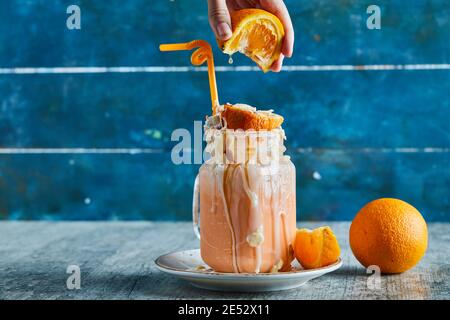 A woman hand squeezing an orange in smoothie and slice of orange on white plate Stock Photo