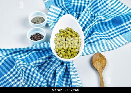 Boiled green peas in a white bowl on a white background with spices, a spoon, and a tablecloth Stock Photo