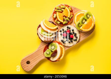 Crispy puffed rice cakes on board with fresh fruit kiwi banana apple blueberries raspberries and orange on the yellow background - top view on healthy Stock Photo