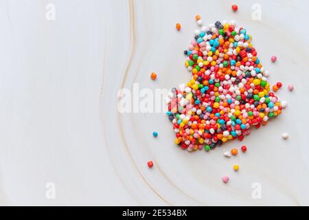 Creative holiday concept of love. Heart shape made from small colorful candies on a white marble background. Valentine's Day concept. Top view, flat lay. High quality photo Stock Photo