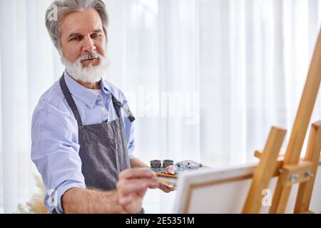 senior grey haired artist man painting using painter palette and canvas, at home, work as hobby Stock Photo