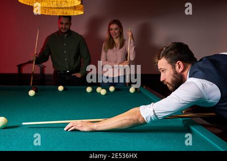 man leaning over the table while playing snooker, he is concentrated on game, having leisure time Stock Photo