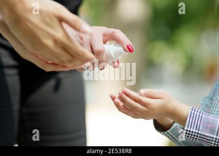 Close-up family applying hand sanitizer to clean and disinfect hands outdoors. Woman applying spray against virus. Stock Photo