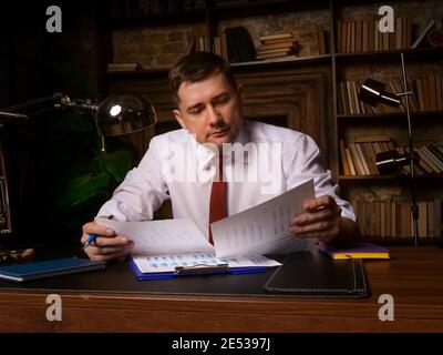 Male businessman works with business reports and financial charts. Paperwork late at night. Stock Photo