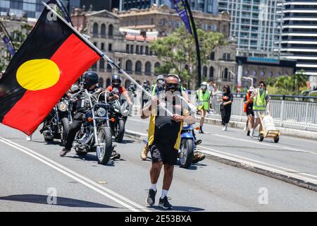 A protester waves the Aboriginal Flag across Victoria Bridge during the march. Crowds of people gathered in Brisbane, Queensland to protest against the Australia public holiday, which is a date synonymous with the beginning of many decades of persecution of Indigenous Australian people by the British colonialists. The protesters instead referred to the date as Invasion Day, to signify the invasion of Aboriginal lands by British colonisers, beginning with the First Fleet in 1788. Many policies stem from the harsh early days such as overwhelming incarceration of Aboriginal people, as well as man Stock Photo