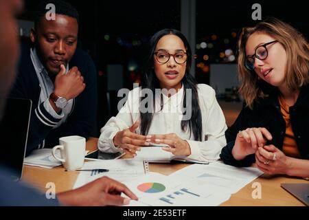 Young Group of multi ethnic business team analyzing financial documents with each other at night before a deadline Stock Photo
