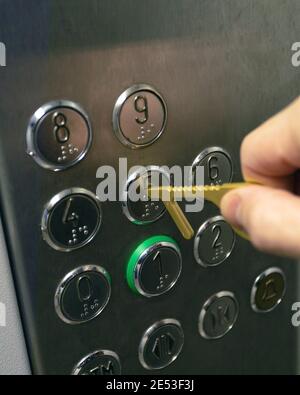 Man using brass key grip to press buttons without touching them to avoid spread of coronavirus disease. Stock Photo