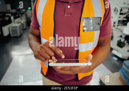 Midsection of a african american male factory worker typing on digital tablet in factory Stock Photo