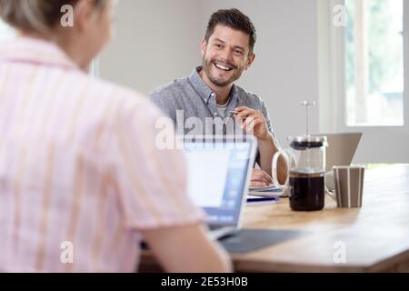Business Couple Working From Home Sitting At Table During Pandemic Lockdown Stock Photo